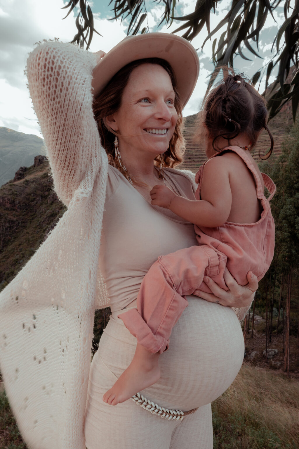 Nalaya, smiling in a straw hat, holding her daughter in the Sacred Valley of Peru