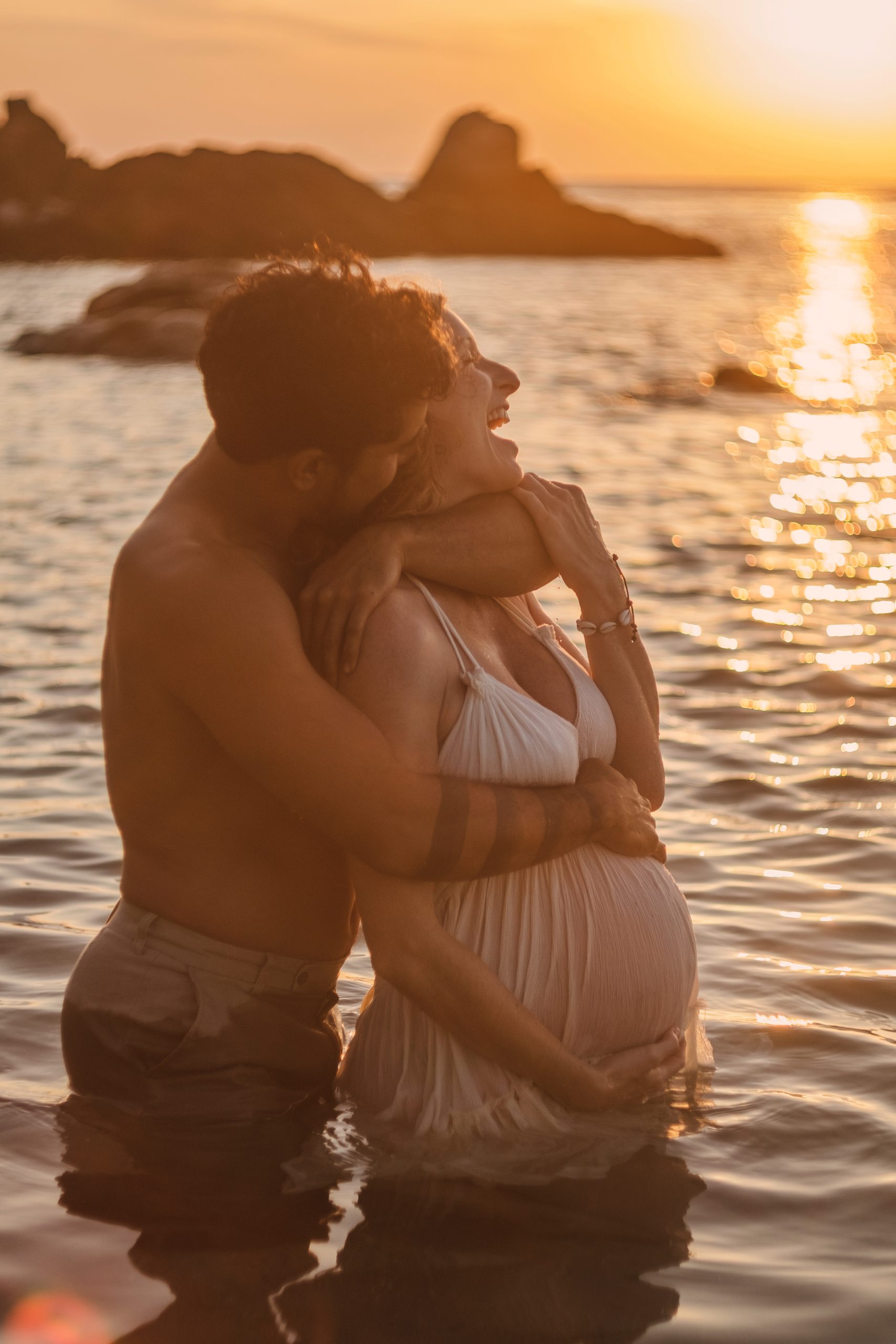 Pregnant couple ocean embrace laughter